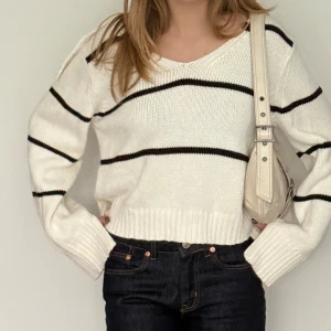 Vit stickad tröja med krage från Lindex - Superfin vit stickad tröja från Lindex med svarta horisontella ränder och bred krage. Tröjan har v-ringning, lång ärm och ribbade muddar. Perfekt till jeans för en chill och snygg look.