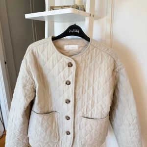 Beige quiltad jacka från Zara XS - Quiltad beige jacka från Zara i storlek XS. Jackan har rund halsringning, stora snygga bruna knappar framtill och två fickor. Den är knappt använd bara några få gånger så den är som ny, inga defekter. 