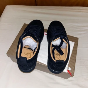 Mörkblå Christian Louboutin sneakers - Snygga svarta sneakers från Christian Louboutin i mocka med klassisk röd sula och broderad logga på hälen. Skorna har rund tå, svarta skosnören och beige innersula. Perfekta för dig som vill ha en stilren och lyxig look.