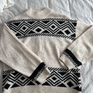 Beige och svart stickad polotröja ONLY - Snygg stickad polotröja från ONLY i beige med svart grafiskt mönster. Tröjan har ribbad hög krage och långa ärmar med mönsterdetaljer vid muddar och nederkant. Passar perfekt nu i höst och vinter. Använd endast en gång. Storlek M 