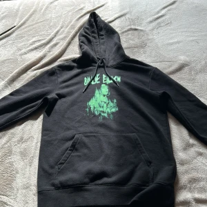 Billie Eilish svart hoodie med tryck - Svart hoodie med grön Billie Eilish-tryck på bröstet. Klassisk känguruficka, huva med snörning och lång ärm. Perfekt för dig som gillar streetstyle och vill sticka ut med en cool artisttröja.
