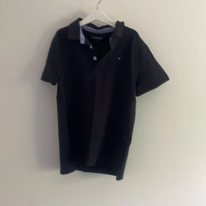 Blå pikétröja Tommy Hilfiger - Klassisk Blå pikétröja från Tommy Hilfiger med korta ärmar och krage. Tröjan har knappar framtill och en liten broderad logga på bröstet. Tillverkad i mjuk bomull och har diskreta Hilfiger-detaljer vid kragen.