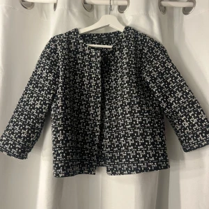 Svartvit rutig kavaj från Zuiki - Stilren svartvit kavaj från Zuiki med rutigt mönster och grov textur. Jackan har rund halsringning, lång ärm och stängs med en knapp framtill. Perfekt för dig som gillar klassisk men trendig look.