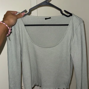 Ljusgrön ribbad långärmad topp - Säljer en ljusgrön ribbad topp med lång ärm och rundad, djup urringning. Toppen är croppad med vågig kant nertill och har vida armar. 