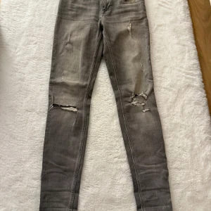 Grå skinny jeans med slitningar - Säljer ett par grå skinny jeans från Denim 1975 med snygga slitningar och hål på knäna. Jeansen har en tight passform och klassisk femficksdesign. Perfekta för dig som gillar en edgy och trendig look.