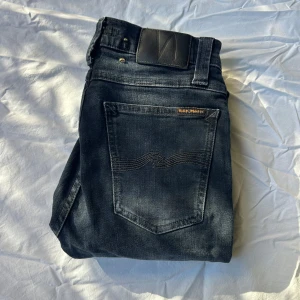 Nudie Jeans High Kai W28 L32 - Snygga svarta jeans från Nudie Jeans, modell High Kai. Jeansen har en använd tvätt, klassisk femficksdesign och dragkedja. Tillverkade i 98% ekologisk bomull och 2% elastan för en bekväm passform. Perfekta för dig som gillar stilrena och bekväma jeans.