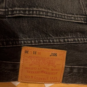 Levi's 501 svarta jeans W31 L30 - Svarta Levi's 501 jeans med klassisk rak passform och fem fickor. Jeansen har snygga kopparfärgade nitar och Levi's Premium-märke bak. Tillverkade i robust denim som ger en tidlös look.
