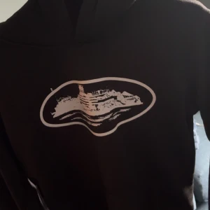 Svart hoodie med skeppstryck köpte på plick så vet ej om den är äkta - Svart hoodie med vitt tryck av ett skepp på bröstet. Klassisk huva och långa ärmar, perfekt för dig som gillar streetstyle och vill ha något unikt i garderoben. Mjuk och skön, passar till chill dagar eller när du vill sticka ut lite extra.