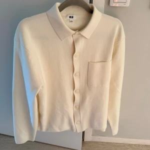 Uniqlo kofta  - Stilren beige kofta från Uniqlo med klassisk krage, knäppning framtill och en bröstficka. Långärmad och i mjukt material som passar perfekt till lager-på-lager. Enkel och clean design som funkar till många outfits.