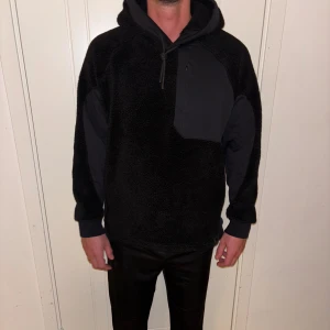 Svart fleece hoodie Colmar Revolution Medium - Svart hoodie från Colmar Revolution x Yosuke Aizawa med mjuk fleece, stora paneler i tyg och bröstficka med dragkedja. Oversized fit, huva med snörning och långa ärmar. Perfekt för kalla dagar och riktigt snygg streetstil. Nypris : 2800