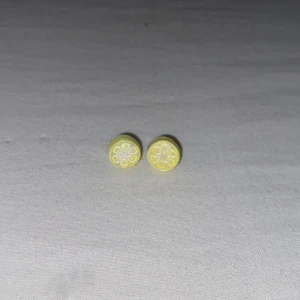 Gula citronskivor örhängen - Söta små örhängen formade som citronskivor i gul och vit färg. Perfekta för dig som vill ha en lekfull och unik detalj till din stil. Runda och färgglada, passar dig som gillar fruktiga accessoarer.