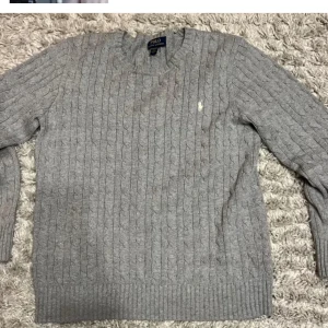 Grå kabelstickad tröja  Ralph Lauren - Kabelstickad grå tröja från Polo Ralph Lauren i storlek XL i barn som är som xs-s passar ca 165-174. Klassisk design med rund halsringning, ribbade muddar och ikoniska broderade loggan på bröstet. Perfekt för lager-på-lager och chill höst- och vinterstil. Kan gå ner i pris vid snabb affär 
