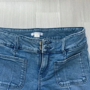 Blå bootcut jeans från Gina Tricot - Snygga ljusblå bootcut jeans från Gina Tricot med låg, dubbla knappar och framfickor. Jeansen har markerad söm längs benen och klassiska bakfickor. Perfekta för dig som gillar en retroinspirerad look.