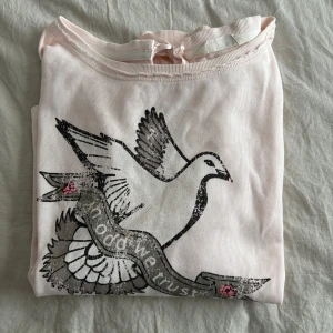 Ljusrosa Odd Molly tröja med tryck - Supersöt ljusrosa långärmad tröja från Odd Molly med tryck av en duva och texten 'in odd we trust' framtill. Tröjan har ribbade muddar, slitsar i sidorna och en fin rosett i nacken. Storlek 1 skulle säga att de motsvarar S-M