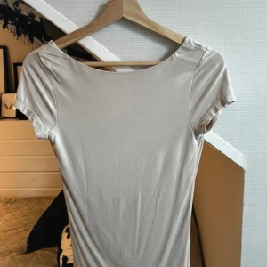 Beige topp/tröja med öppen rygg - Supersnygg beige tröja/topp med båthals och djup öppen rygg. Toppen har korta ärmar och är figurnära i modellen. Perfekt för dig som gillar en enkel men ändå stilren look. Materialet känns mjukt och följsamt mot kroppen.