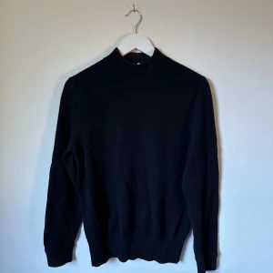 Mörkblå polotröja från Arket i ullmix - Klassisk mörkblå polotröja från Arket i en skön blandning av ull och bomull. Tröjan har lång ärm, ribbade muddar och hög hals. Perfekt för lager-på-lager och enkel att matcha med allt i garderoben. 3S3
