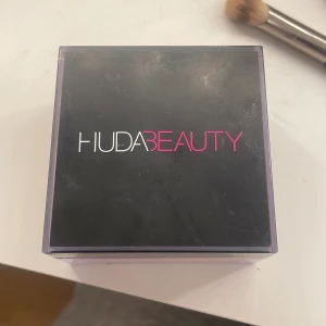Huda Beauty Cherry Blossom Cake puder - Cherry Blossom Cake Easy Bake är ett löst settingpuder i en ljusrosa nyans. Kommer i en fyrkantig transparent burk med svart lock och rymmer 20g. Perfekt för att sätta sminket och ge en mjuk finish. Pudret är superfint och lätt att applicera.