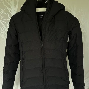 Svart dunjacka från Everest - Svart dunjacka från Everest med huva och hel dragkedja framtill. Jackan har två sidofickor med dragkedja. 