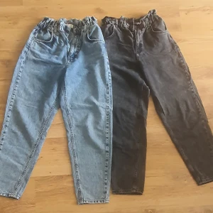 2 par Gina Tricot jeans, storlek 38 - Två par jeans från Gina Tricot i storlek 38. Ena paret är ljusblått och det andra är mörkgrått, båda med resår i midjan och avslappnad passform. Klassisk femficksmodell i mjukt denimtyg, perfekta för en chill och trendig look.