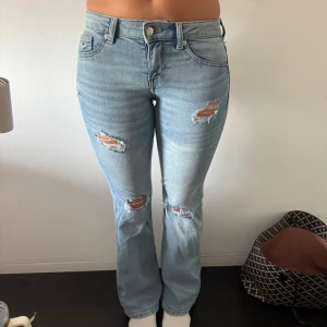 Ljusblå slitna bootcut jeans - Snygga ljusblå jeans med slitningar på låren och knäna. Modellen har bootcut-ben och klassisk femficksdesign. Perfekta för en avslappnad och trendig look. Har aldrig använt jeansen, hålen är egengjorda