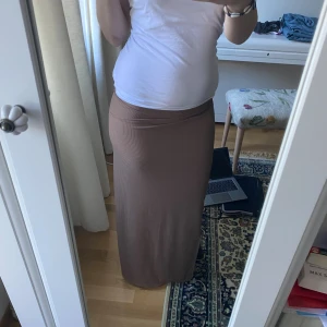 Brun ribbad långkjol - Säljer en brun ribbad långkjol med smal passform. Kjolen har en enkel och stilren design med diskreta ribbade ränder och en liten slits i sidan. Perfekt för dig som gillar en clean och avslappnad look.