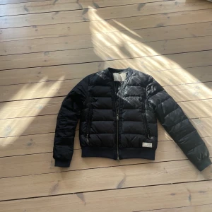 Svart pufferjacka från Odd Molly - Säljer en svart pufferjacka från Odd Molly, modell Hermosa Jacket. Jackan har quiltad design, två dragkedjeförsedda fickor och ribbade muddar. Snygg och stilren med detaljer som Odd Molly-märke och metallhänge vid dragkedjorna. Perfekt för kyligare dagar.