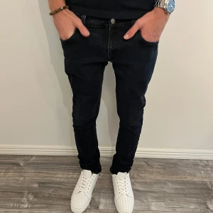Nudie Jeans Long John slim jeans - Slimmade svarta jeans från Nudie Jeans modell Long John. Tillverkade i 98% ekologisk bomull och 2% elastan för extra stretch. Klassisk femficksdesign med broderad bakficka och svart läderpatch i midjan. Snygg, tidlös look med smal passform.