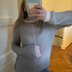 Ljusgrå stickad tröja från Zara - Supermysig ljusgrå stickad tröja från Zara med ljusrosa ribbade muddar och krage. Tröjan har en relaxed fit och långa ärmar, perfekt för lager på lager under kyliga dagar. Enkel och stilren design som är lätt att matcha.