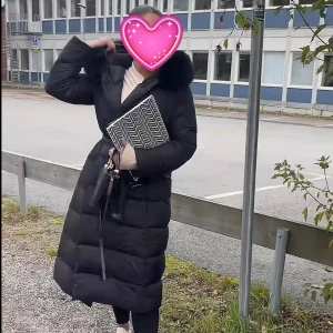 Lång svart dunjacka med pälskrage S - Säljer en lång svart dunjacka med stor fluffig pälskrage och markerad midja. Jackan är quiltad och har en snygg, stilren look som håller dig varm under kalla dagar. Perfekt för dig som vill ha en trendig och bekväm vinterjacka.