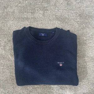Mörkblå stickad tröja från GANT - Klassisk mörkblå stickad tröja från GANT med rund halsringning och broderad logga på bröstet. Tröjan är i bra skick. Pris kan diskuteras.