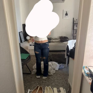 Mörkblå bootcut jeans med slitningar - Säljer ett par mörkblå jeans med bootcut-modell och snygga slitningar på låren och knäna. Jeansen har klassisk femficksdesign och låg midja. Perfekta för dig som gillar en avslappnad men trendig look.