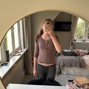 Brun kofta med pärlknappar från Bik Bok - Superfin brun kofta från Bik Bok med pärlknappar hela vägen framtill. Modellen är figurnära med trekvartsärm och rund halsringning. Perfekt att styla med jeans eller kjol.