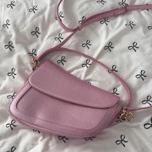 Rosa axelväska från Even&Odd - Säljer en superfin rosa axelväska från Even&Odd med justerbar rem och guldfärgade metalldetaljer. Väskan är i syntetmaterial med struktur och har magnetlås samt innerfack med dragkedja. Perfekt storlek för det viktigaste och snygg att bära crossbody.