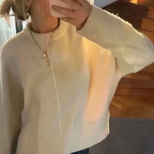 Beige stickad tröja med hög hals - Säljer en beige stickad tröja med hög hals och långa ärmar. Tröjan har en rak passform och synlig söm framtill som ger en snygg detalj. Perfekt för lager-på-lager under kyliga dagar. Den är lite nopprig men inget mer än så!! Pris kan diskuteras 