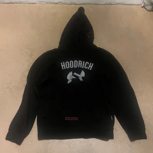 Svart hoodie från Hoodrich med tryck - Svart hoodie från Hoodrich med stor vit logga och duvor på bröstet. Baksidan har tryck med vita duvor och röd text 'From Nothing To Something'. Huva och ribbade muddar. Perfekt för dig som gillar streetwear och vill sticka ut.