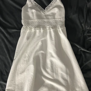 Vit spetsklänning från Loness - Superfin vit kortklänning från Loness med tunna axelband och v-ringning. Klänningen har vackra spetsdetaljer och broderier vid bysten och midjan, samt lätt strukturerat tyg. Perfekt för sommarens alla tillfällen!