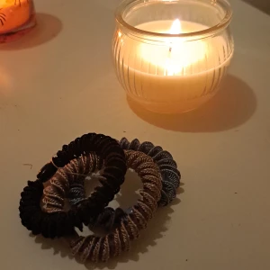 Tre spiralformade armband i olika färger - Säljer ett set med tre spiralformade armband i svart, beige och gråblå. Armbanden är elastiska och har en glansig yta med dekorativa pärldetaljer. Perfekta att mixa och matcha till olika outfits.