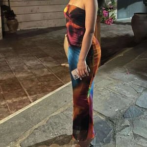 Färgstark lång bandeauklänning - Säljer en supercool lång bandeauklänning med färgstarkt mönster i blått, orange, rött och svart. Klänningen är figurnära och axelbandslös, perfekt för dig som vill sticka ut. Materialet känns mjukt och följsamt mot kroppen.