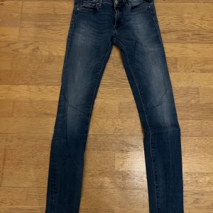 Replay Luz skinny jeans blå, stl 24 - Snygga Replay Luz jeans i mörkblå tvätt med skinny fit. Klassisk femficksmodell med dragkedja och knapp framtill. Tydliga slitningar och detaljer på fickorna. Perfekta för dig som gillar tajta jeans med modern look.