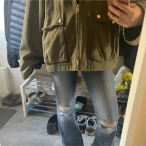 Olivgrön cargojacka med fickor - Säljer en olivgrön cargojacka från Q med två stora fickor framtill och dragkedja. Jackan har en loose passform och är tillverkad i bomull. Perfekt för dig som gillar streetstyle och vill ha en chill look. Kragen är mörkare och ger en snygg kontrast.