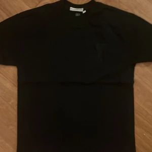 Svart t-shirt från Ami Paris med hjärtdetalj - Svart t-shirt från Ami Paris i storlek S. Klassisk modell med kort ärm och rund hals. På bröstet finns Ami:s ikoniska hjärta med A-broderi. T-shirten är gjord i mjuk bomull och har en clean, stilren vibe.