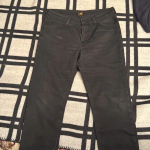 Svarta jeans från Lee, straight fit - Svarta jeans från Lee med klassisk femficksdesign och raka ben. Jeansen har Lee-logga på knapp och bakficka, samt bälteshällor och dragkedja. Materialet är slitstarkt denim i bomull och passformen är straight, perfekt för en clean och enkel look.