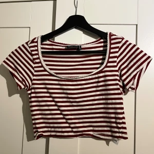 Randig croppad topp från Gina Tricot - Säljer en croppad topp från Gina Tricot med röda och vita ränder. Toppen har korta ärmar, rundad hals med söt spetskant och är gjord i mjuk bomull. Perfekt för dig som gillar retrovibbar och vill ha en chill look.