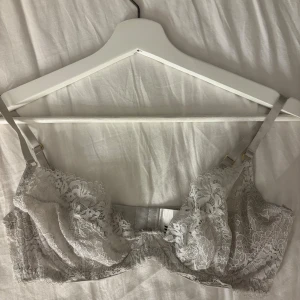 Vit spetsblus från H&M med justerbara band - Säljer en vit blus från H&M i storlek 80C, gjord i mjuk spets med blommigt mönster. Blusen har justerbara axelband och hakknäppning bak. Materialet är polyamid och elastan, vilket gör den både stretchig och bekväm. Perfekt för dig som gillar romantiska detaljer.