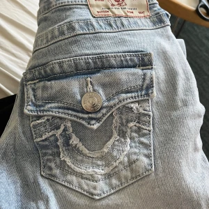 True Religion Joey stl 24 - Ljusblå True Religion jeans i nyskick! Det är modellen Joey som har låg midja och bootcut.  Midja 36cm rakt över Innerbenslängd 85cm Tjejen på bild är 175cm lång