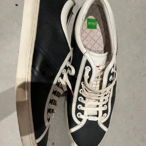 Boss sneakers  - Snygga sneakers från Hugo Boss i svart textil med vita detaljer och snörning. Perfekta för en stilren och clean look. Skivka för med information!
