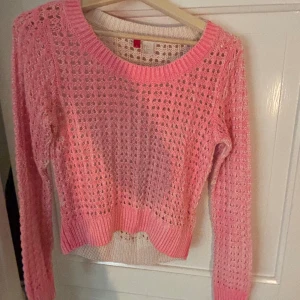 Rosa stickad tröja från H&M - Säljer en söt rosa stickad tröja från H&M i storlek 34. Tröjan har ett hålmönstrat stickat material och ribbad kant vid halsen och nederdelen. Långärmad och perfekt för dig som gillar ljusa färger och mysiga vibes.