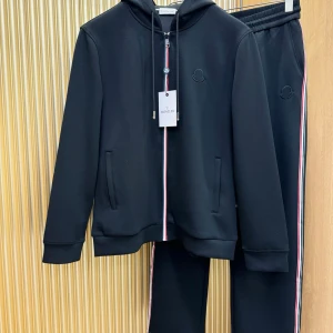 Svart hoodie från Moncler med broderad logga - Svart hoodie från Moncler med broderad logga på bröstet, huva med snörning och dragkedja med röd, vit och blå detalj. Långärmad och med ribbade muddar. Snyggt minimalistisk design och mjukt material som känns lyxigt.