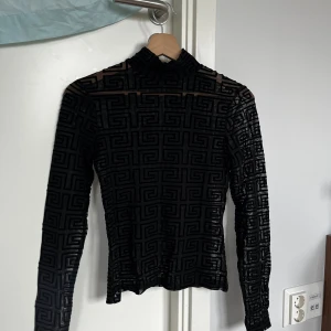 Svart mesh polotopp från Amisu - Säljer en svart mesh polotopp från Amisu i storlek S. Toppen har ett genomskinligt material med ett grafiskt mönster och lång ärm. Hög krage och tight passform ger en cool och edgy vibe. Perfekt för att styla lager på lager eller som statement-piece.