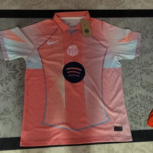 FC Barcelona rosa matchtröja Nike M - Säljer en FC Barcelona fotbollströja från Nike i rosa och ljusblå toner med tryck Lamine Yamal 10 på ryggen. Tröjan har korta ärmar, krage och är tillverkad i lätt, ventilerande Dri-Fit ADV-material. Snygg design med klubbmärke och sponsorlogga framtill.